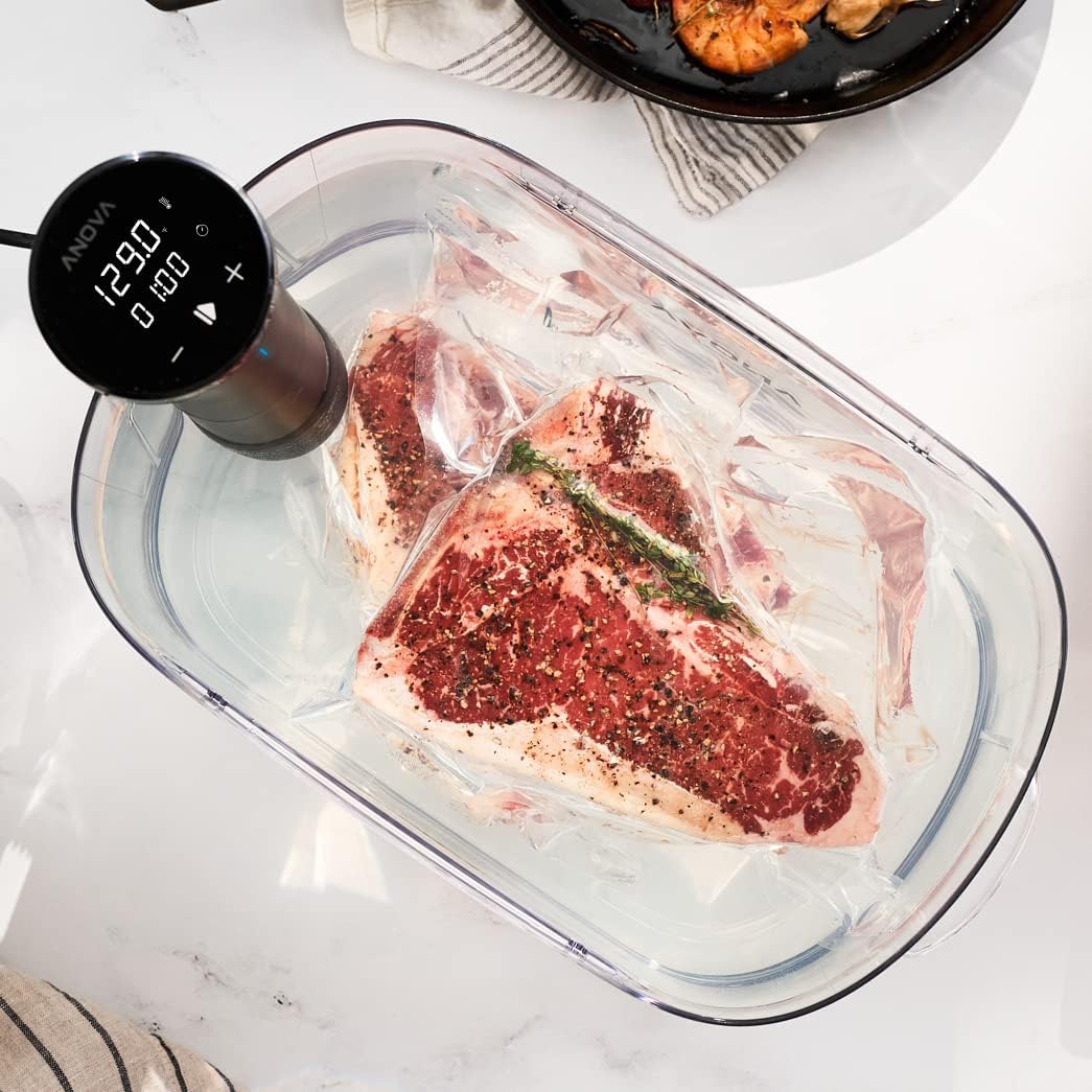 Anova Culinary Sous Vide Precision Cooker Nano clamped to a water bath with steaks cooking