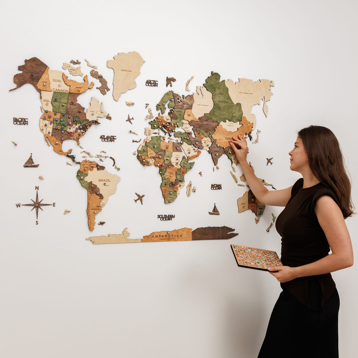 Pinnable 3D wooden world map in Nature wood tones mounted on a white wall with flag pins